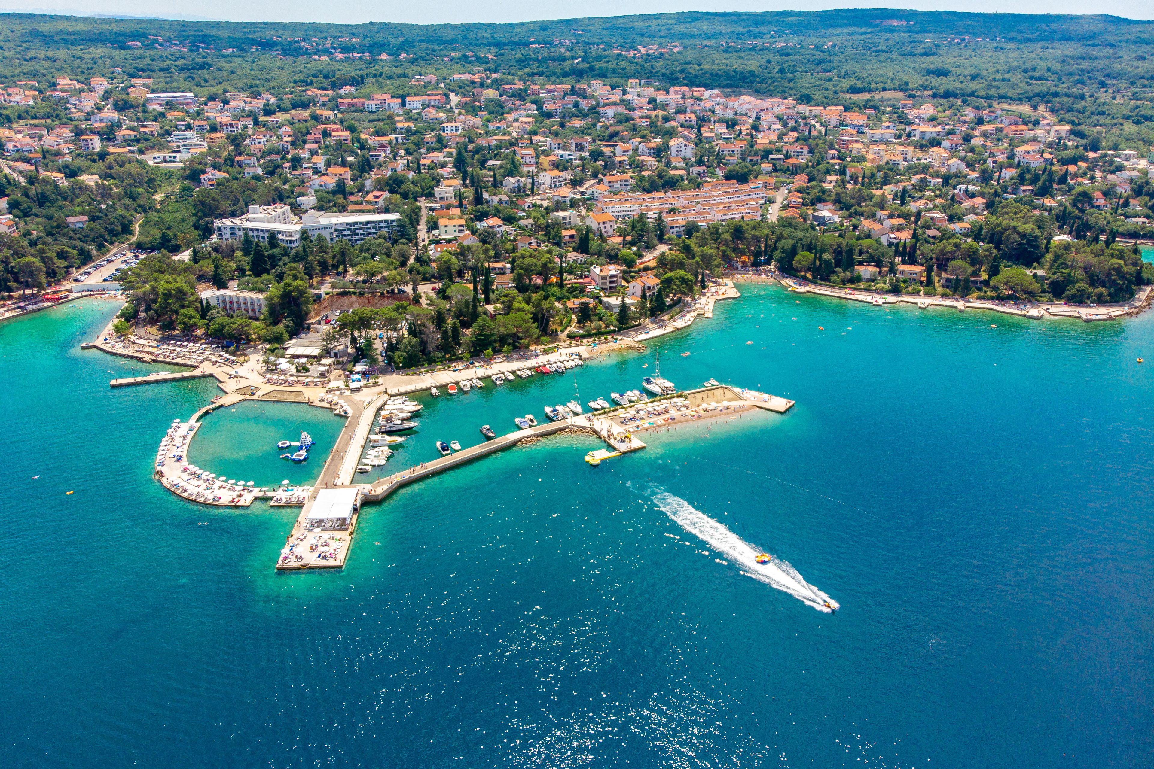 Vue aérienne d’une ville côtière avec un port de plaisance, des bateaux et une jetée.