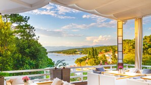 Una terraza con mobiliario de mimbre blanco, vista al mar y follaje.