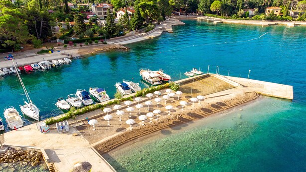 Un puerto deportivo con barcos amarrados, una zona de playa con sombrillas y una vista despejada del paisaje circundante.