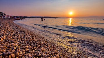 Relax on the beach with comfortable seating and umbrellas, overlooking the calm waters and scenic hills.