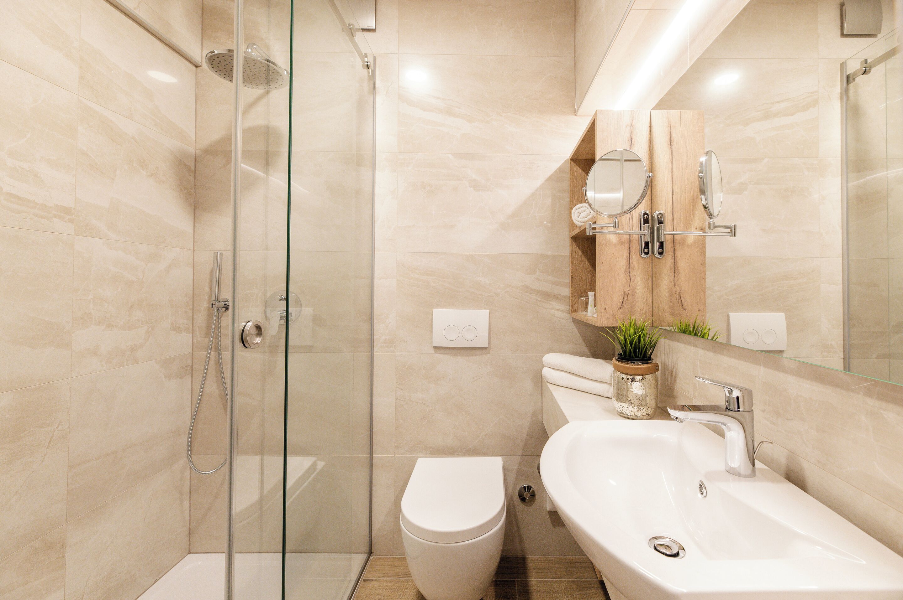 Un baño moderno con cabina de ducha de vidrio, inodoro blanco y lavamanos con espejo superior.