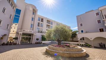 A hotel courtyard with a central fountain, a large tree, and a building with balconies.