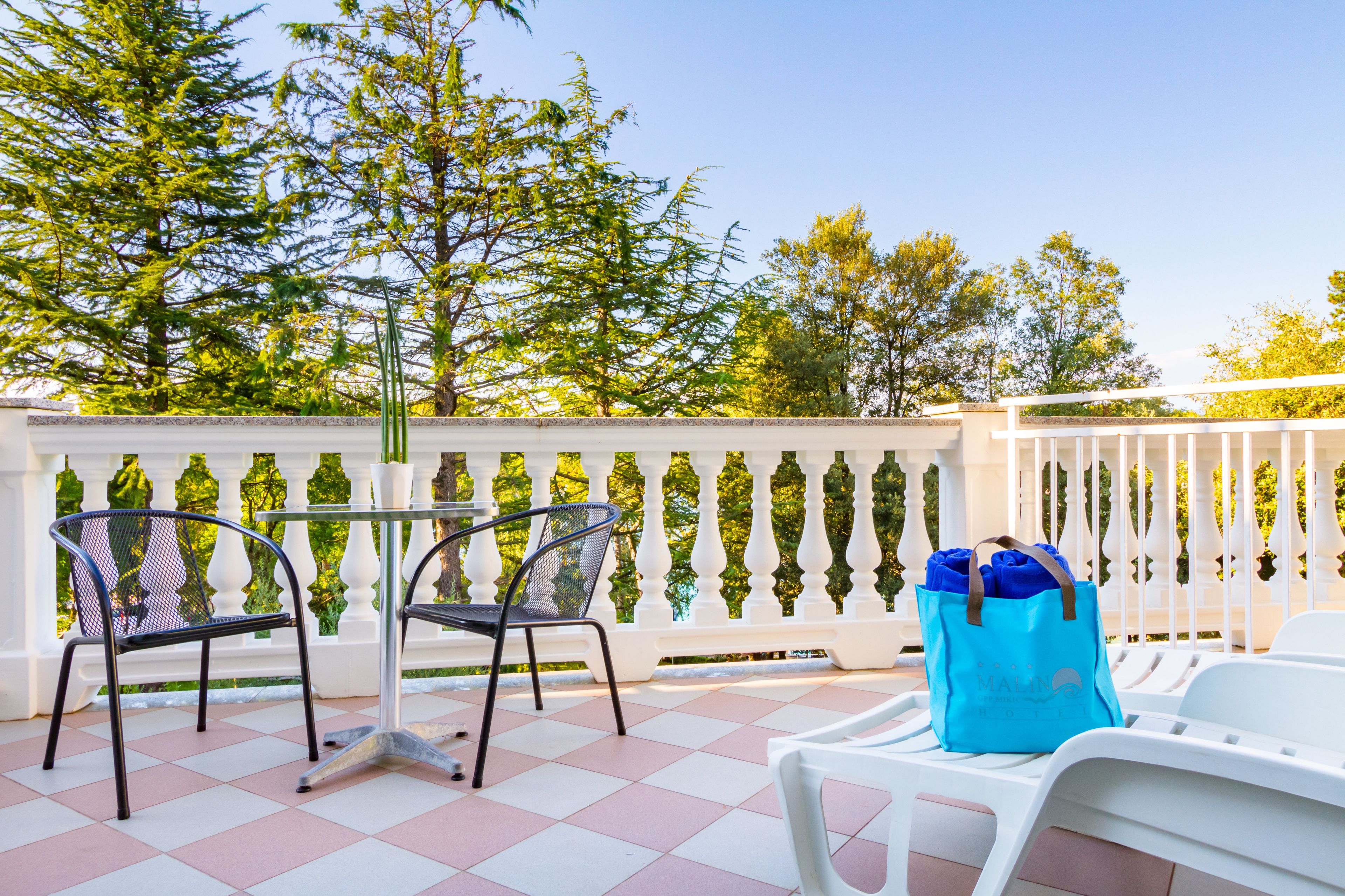 A balcony with two chairs, a table, and a blue bag.