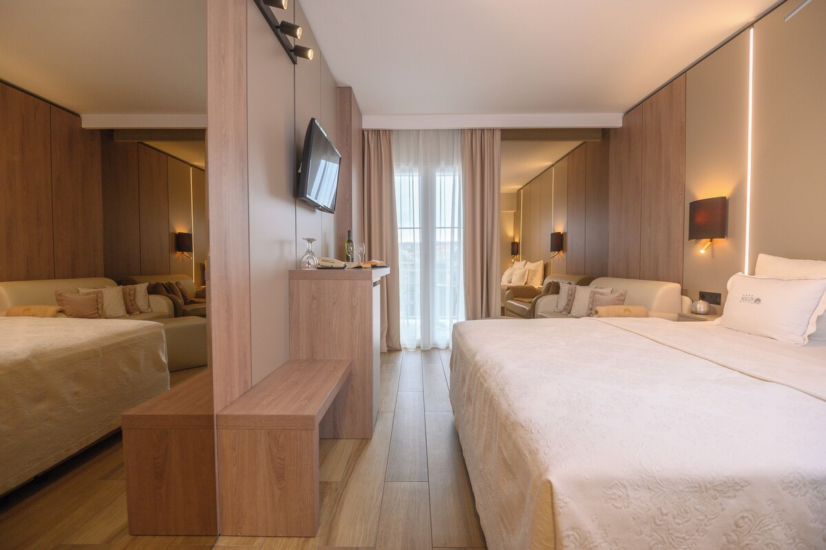 Habitación de hotel con dos camas, televisión, escritorio y un amplio ventanal con cortinas.