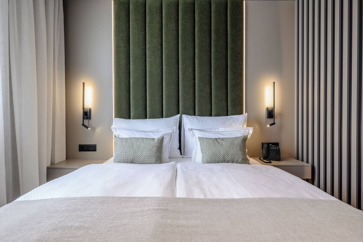 Une chambre d’hôtel avec un grand lit, deux tables de chevet, une tête de lit recouverte d’un tissu vert et un mur à rayures.