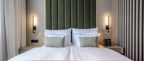 A hotel room with a large bed, two bedside tables, a green upholstered headboard, and a striped wall.