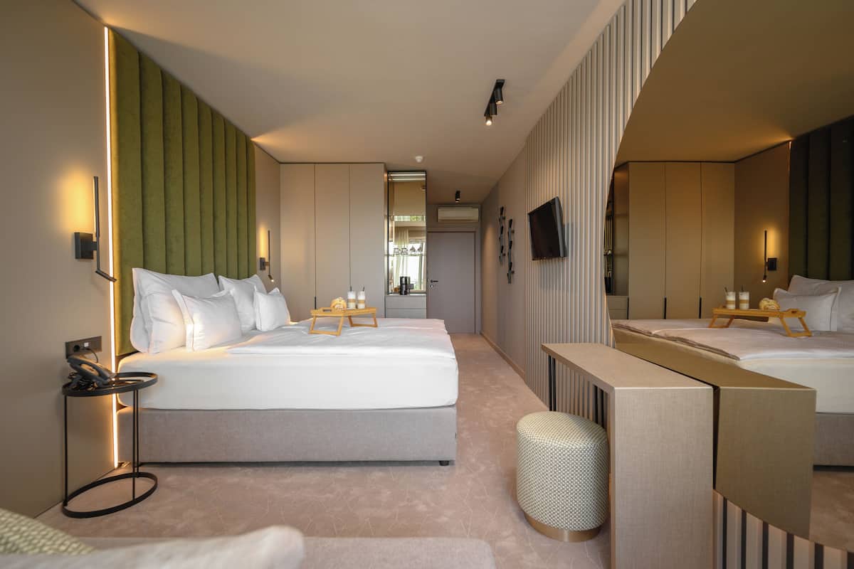 Une chambre d’hôtel moderne avec un grand lit, des tables de chevet, un miroir et un petit coin salon.