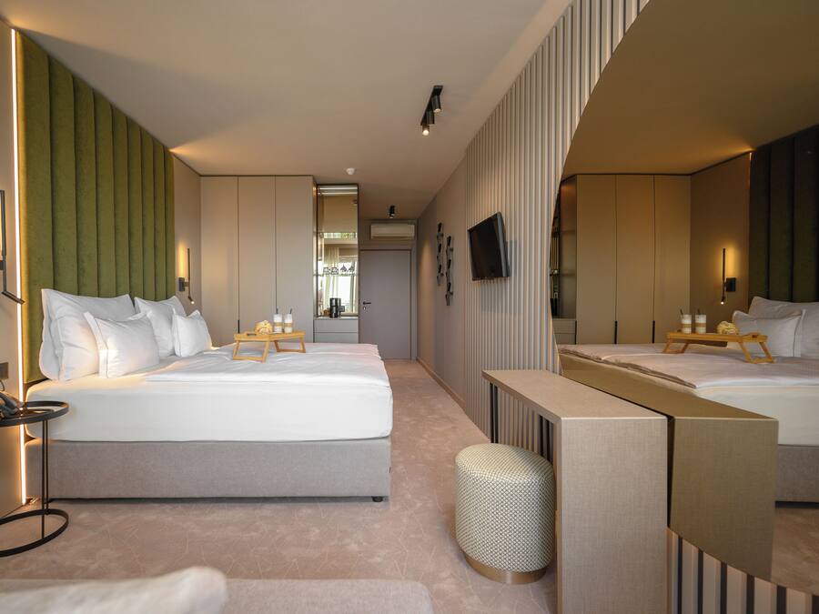 Una habitación de hotel moderna con una cama grande, mesitas de noche, un espejo y un pequeño espacio de descanso.
