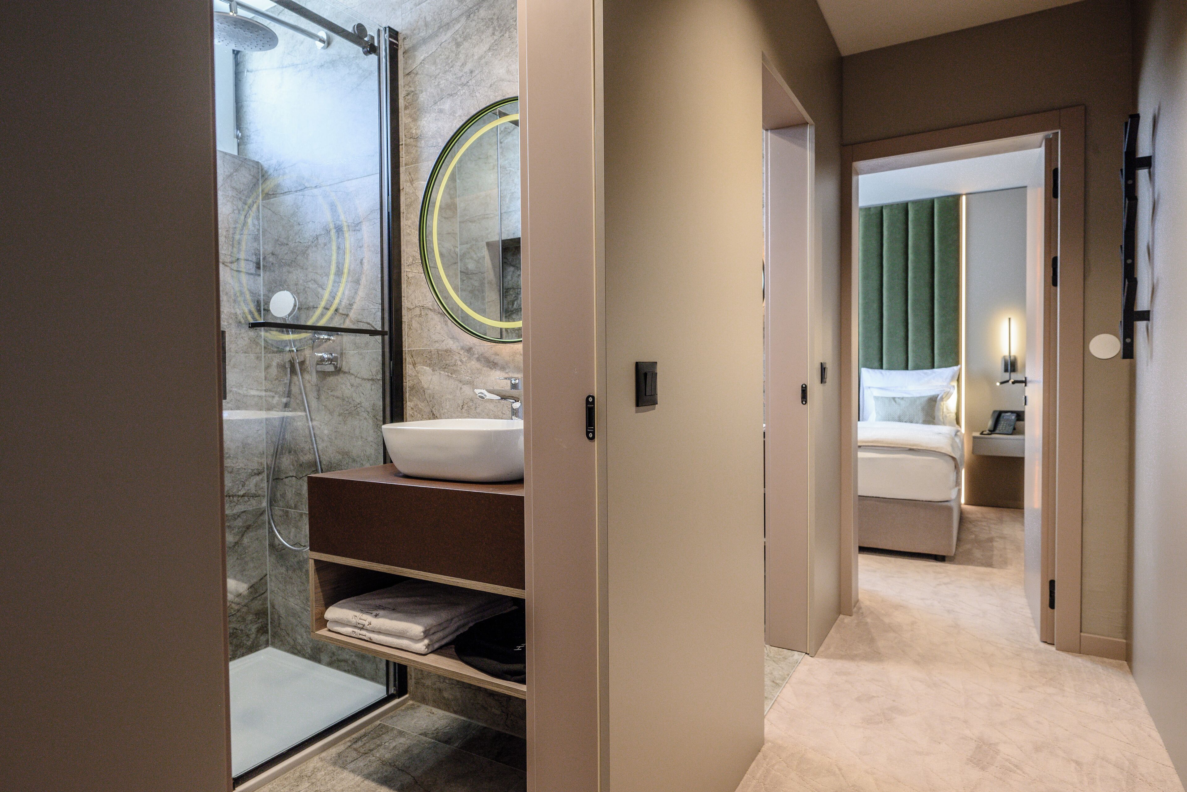 A modern bathroom with a glass shower enclosure, a marble-tiled wall, and a white sink.