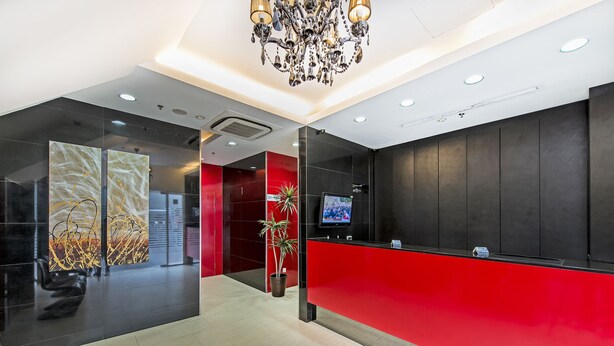 Un espace d’accueil moderne avec un comptoir rouge, des murs noirs et un lustre.