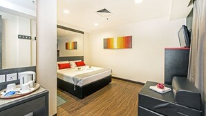 Une chambre d’hôtel avec un lit, un bureau avec un ordinateur, une chaise et une petite table sur laquelle se trouvent une serviette et une fleur.