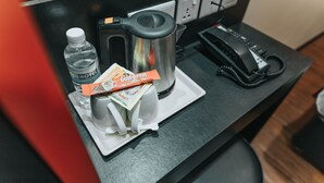 Un mini-bar d’hôtel contenant une bouteille d’eau, une machine à café, un téléphone et un sachet de café moulu Gold Roast.