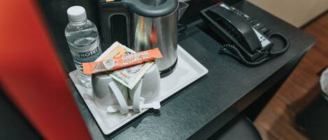 Un mini-bar d’hôtel contenant une bouteille d’eau, une machine à café, un téléphone et un sachet de café moulu Gold Roast.