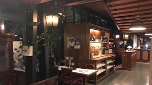 Un restaurante acogedor con mobiliario de madera, una zona de bar y plantas colgantes.
