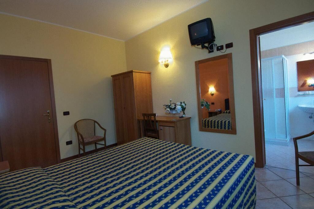 A hotel room with a bed, a desk, a chair, a television, and a mirror.