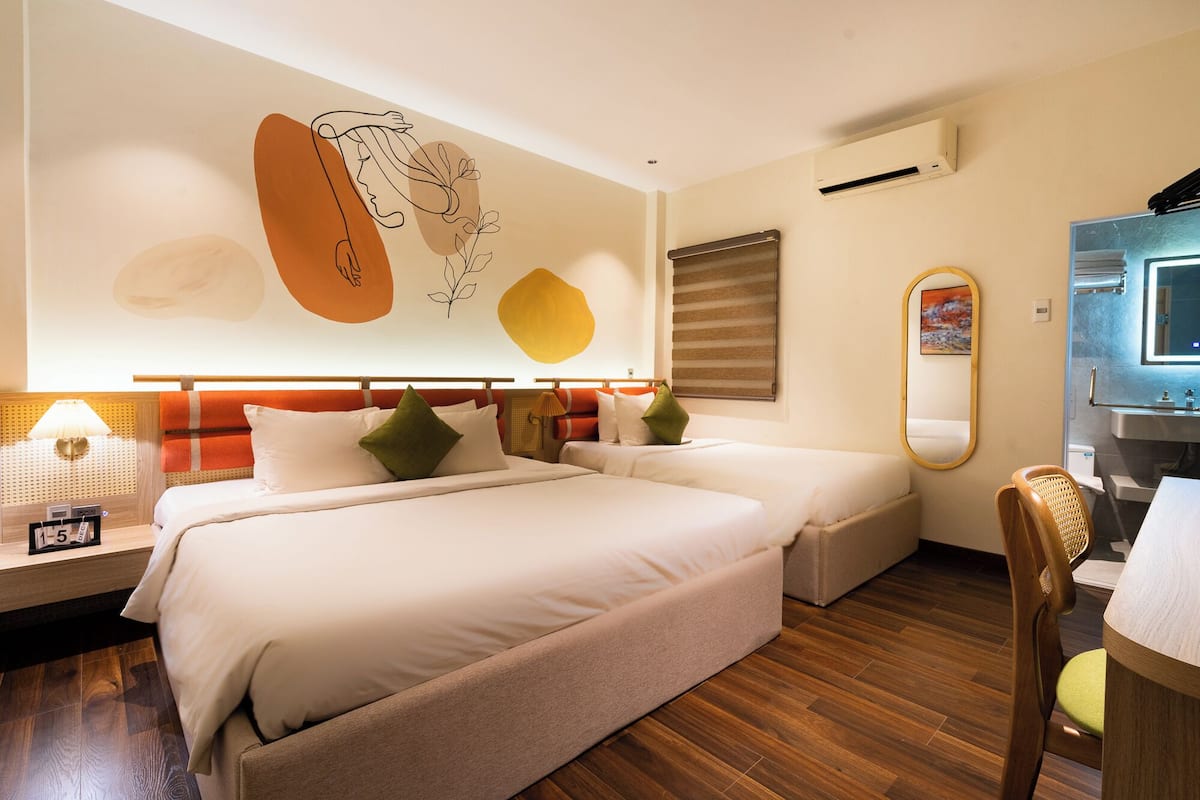Een hotelkamer met twee bedden, een houten vloer, een wandairconditioner, een spiegel en een kleine tafel met een stoel.