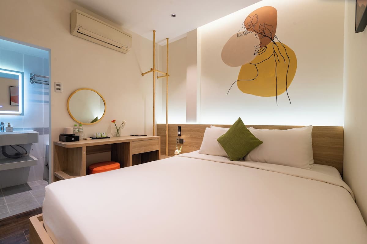 Een moderne hotelkamer met een groot bed, een nachtkastje, een bureau, een spiegel en een wandairconditioner.