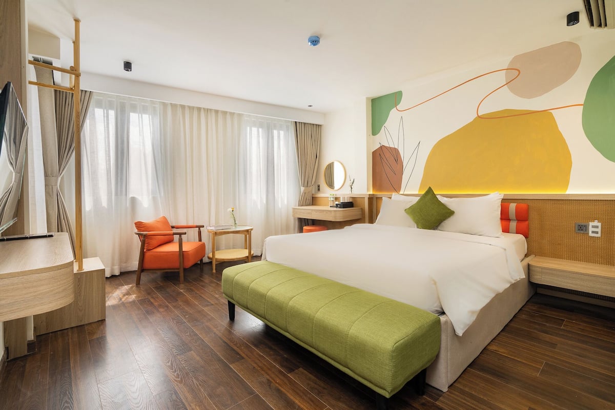 Een moderne hotelkamer met een groot bed, een groene bank, een houten bureau, een stoel en een groot raam met gordijnen.