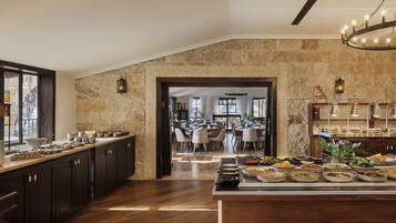 A spacious kitchen with a buffet setup, stone walls, and a view into a dining area.