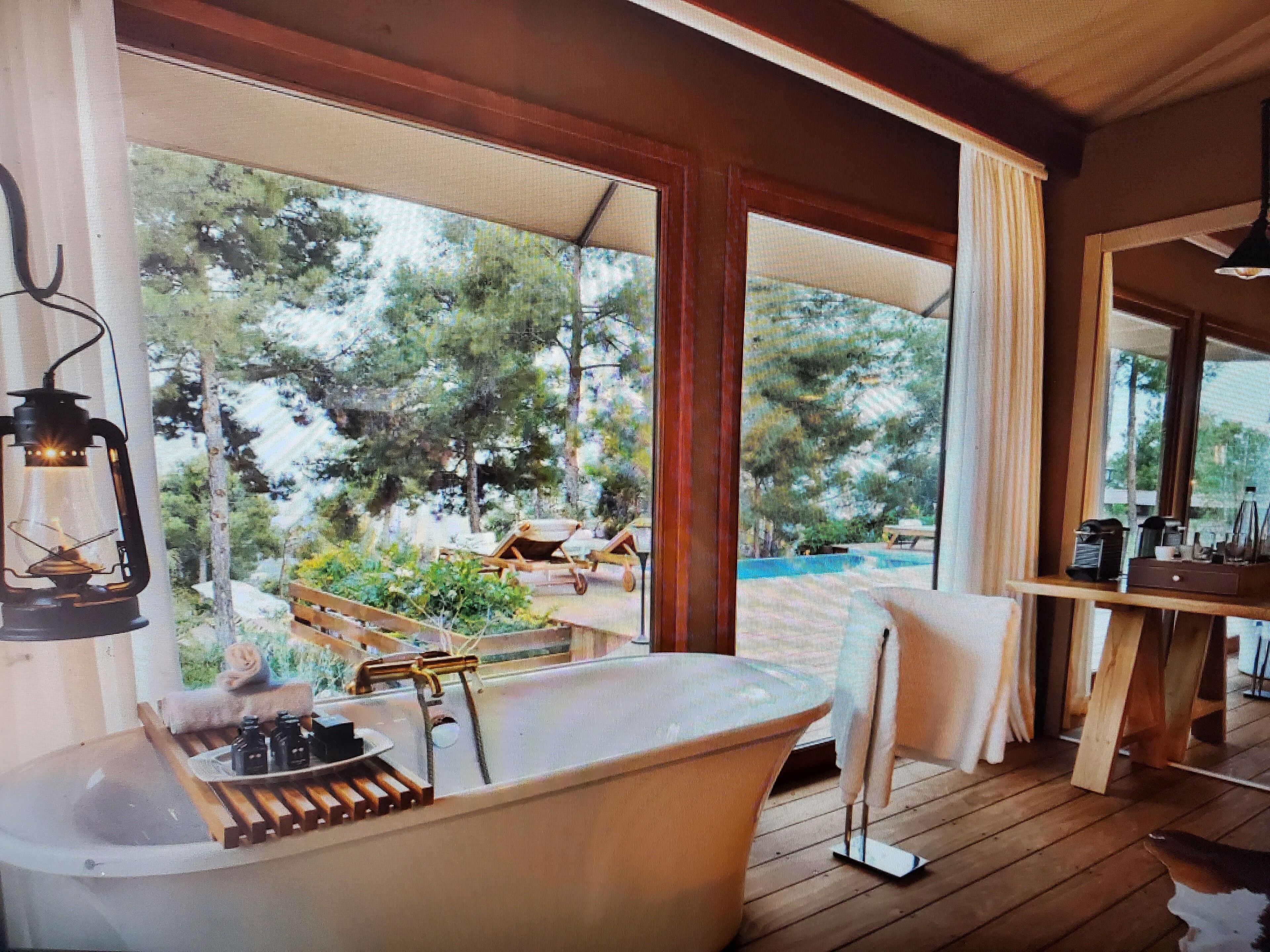 A wooden deck with a bathtub, a wooden chair, and a table with a lamp.