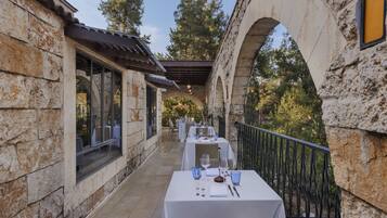 Un espacio de comedor al aire libre con paredes de piedra y una sección cubierta, con mesas dispuestas para comer y sillas.