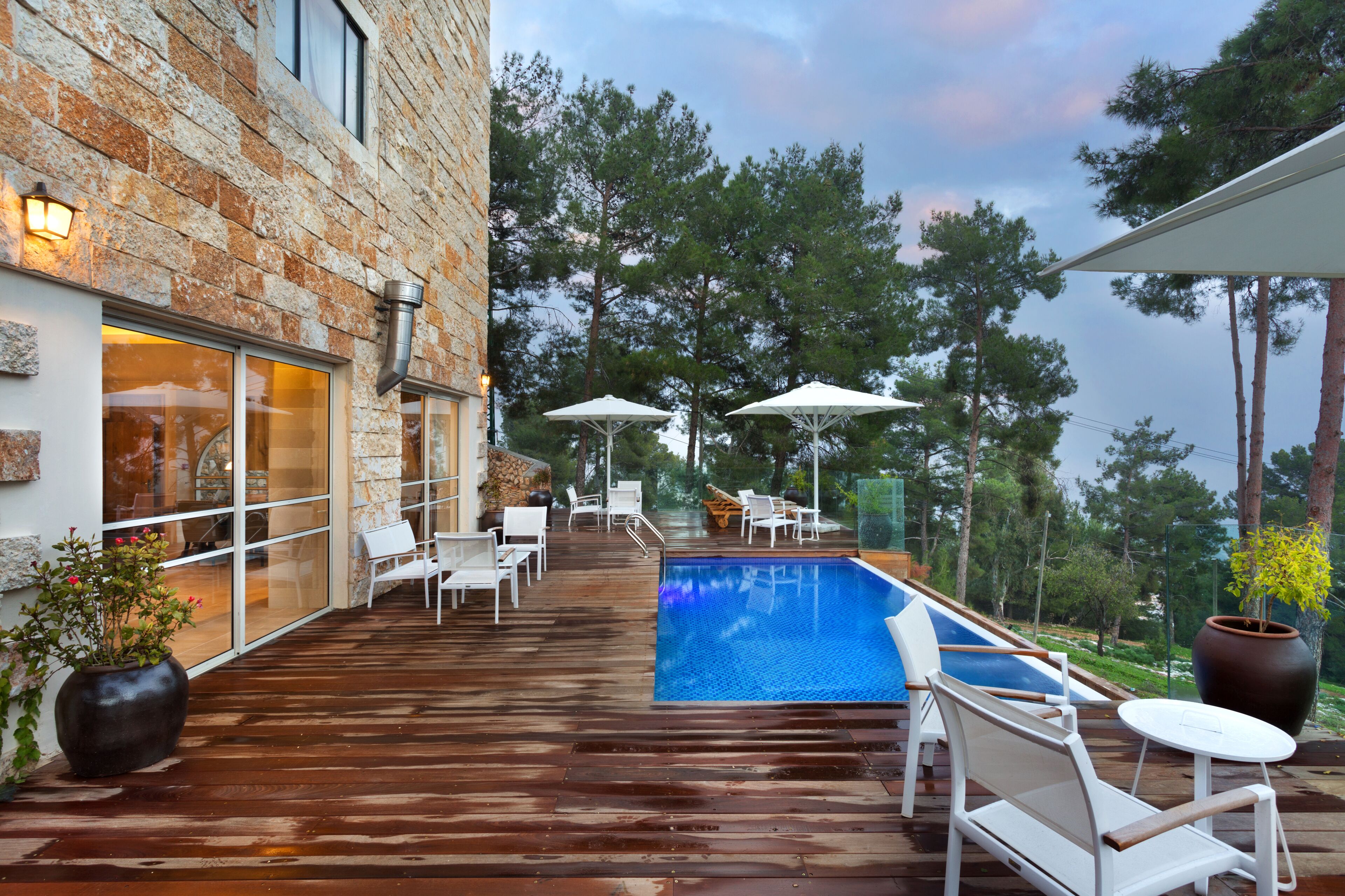 Una terraza de madera con piscina, mobiliario exterior y un edificio de piedra.