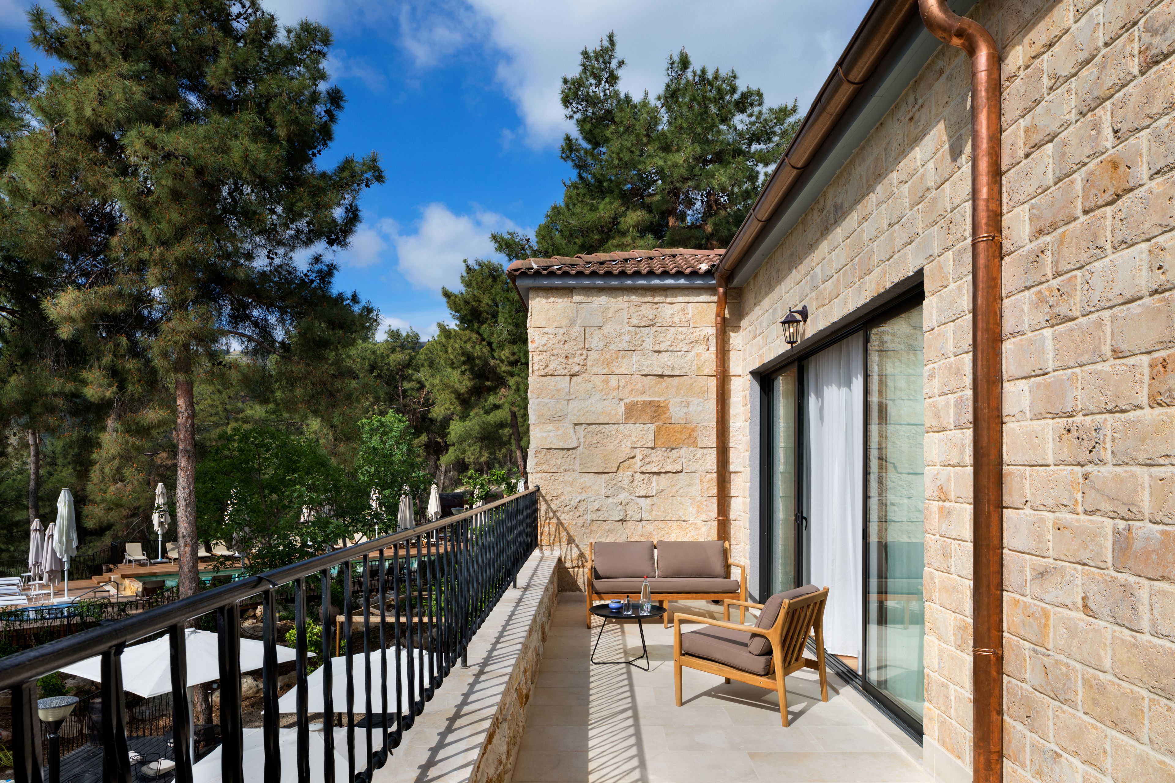 Un balcon aménagé avec du mobilier d’extérieur, un mur en pierre et une vue sur les arbres.