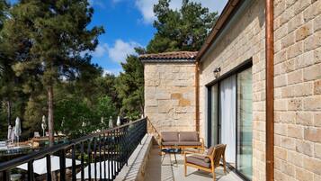 Un balcon aménagé avec du mobilier d’extérieur, un mur en pierre et une vue sur les arbres.