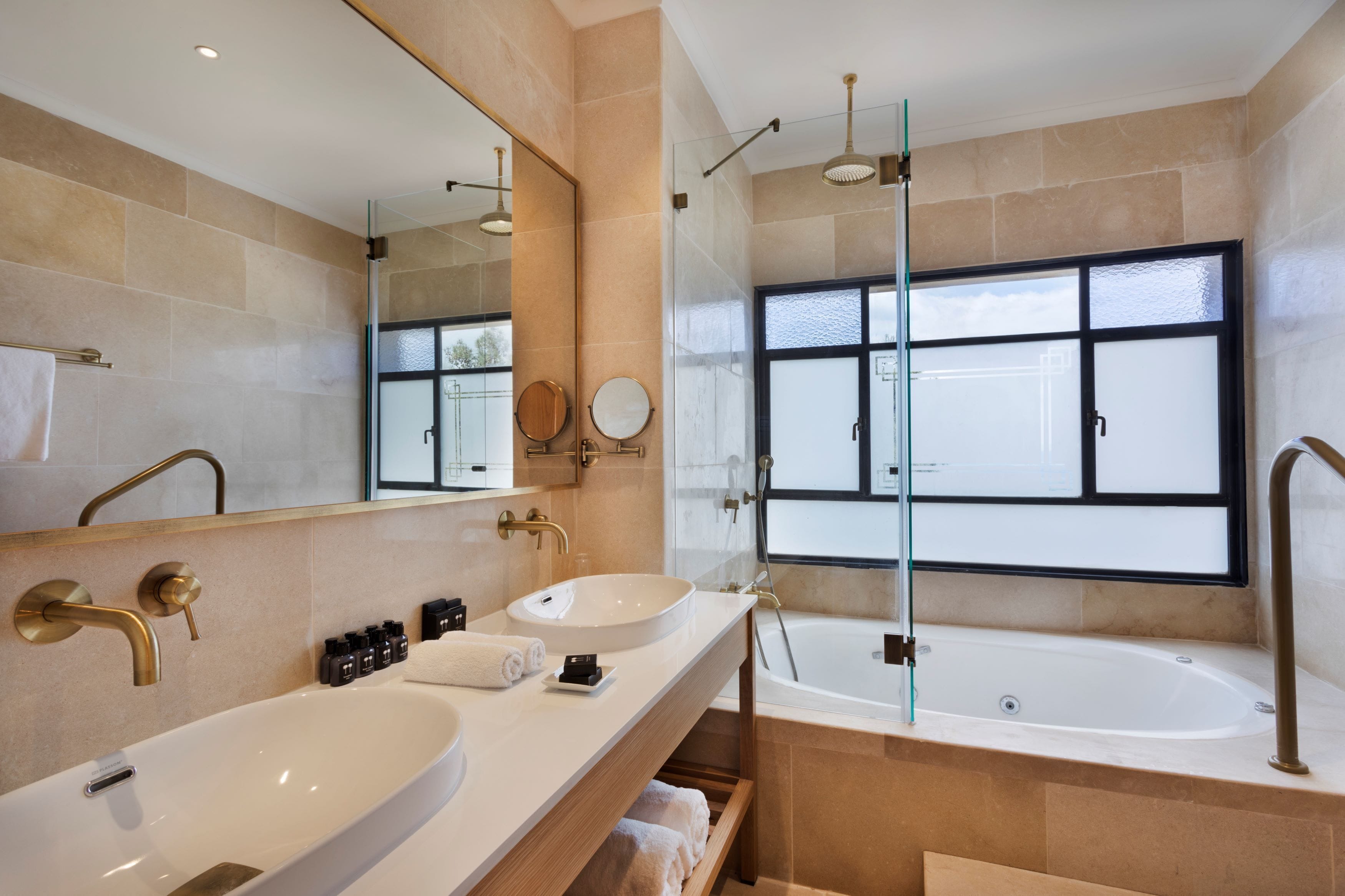 A modern bathroom with two sinks, a large mirror, a bathtub, and a window.