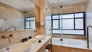 A modern bathroom with two sinks, a large mirror, a bathtub, and a window.
