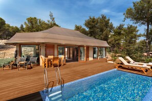 Una terraza de madera con piscina, sillas de descanso y un porche cubierto.