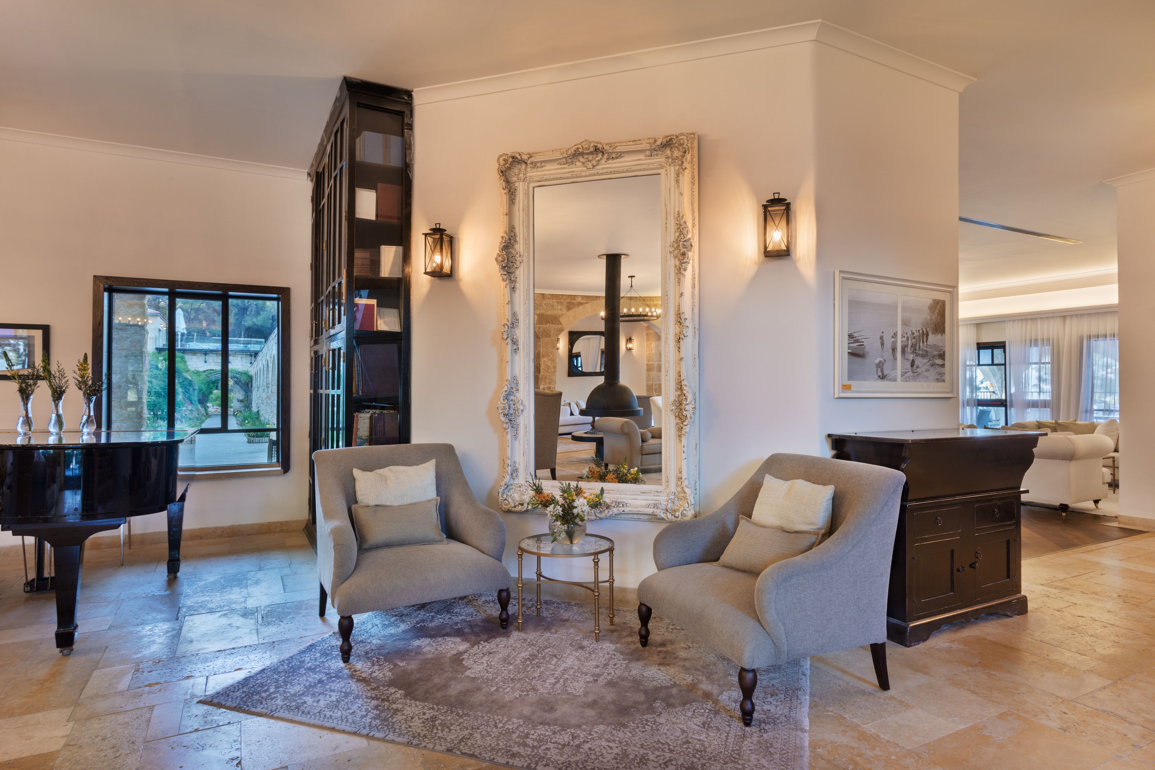 A spacious living room with a grand piano, two armchairs, a large mirror, and a fireplace.