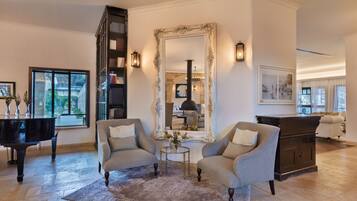A spacious living room with a grand piano, two armchairs, a large mirror, and a fireplace.