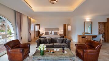 A hotel room with a bed, two leather armchairs, a coffee table with a vase of flowers, and a desk with a mirror.