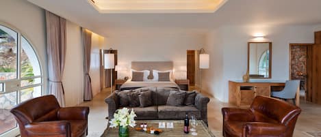 A hotel room with a bed, two leather armchairs, a coffee table with a vase of flowers, and a desk with a mirror.