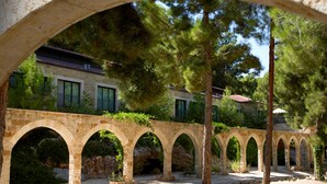An arched stone bridge in a courtyard with a building in the background.