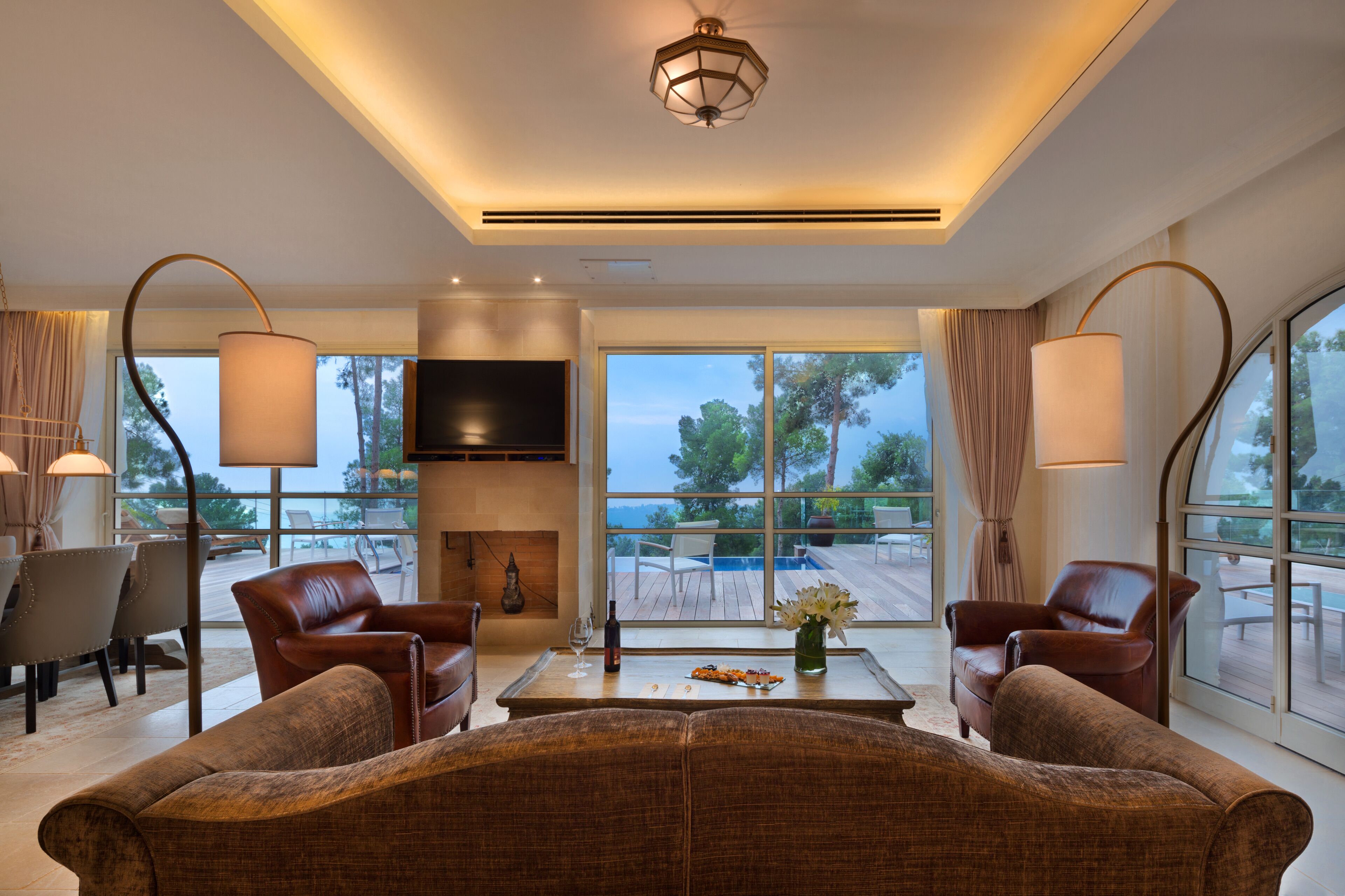 A modern living room with leather sofas, a coffee table with a wine bottle and glasses, and large windows offering a view of the outdoors.