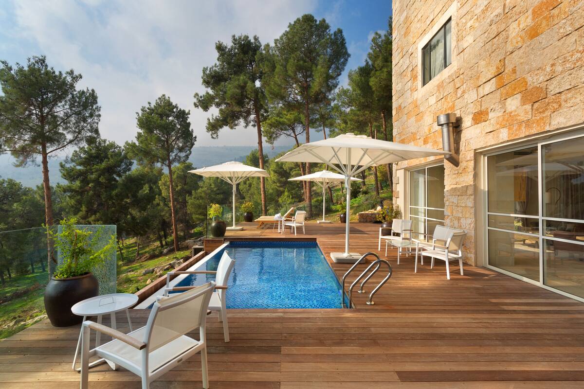 A wooden deck with a pool, white lounge chairs, and umbrellas.