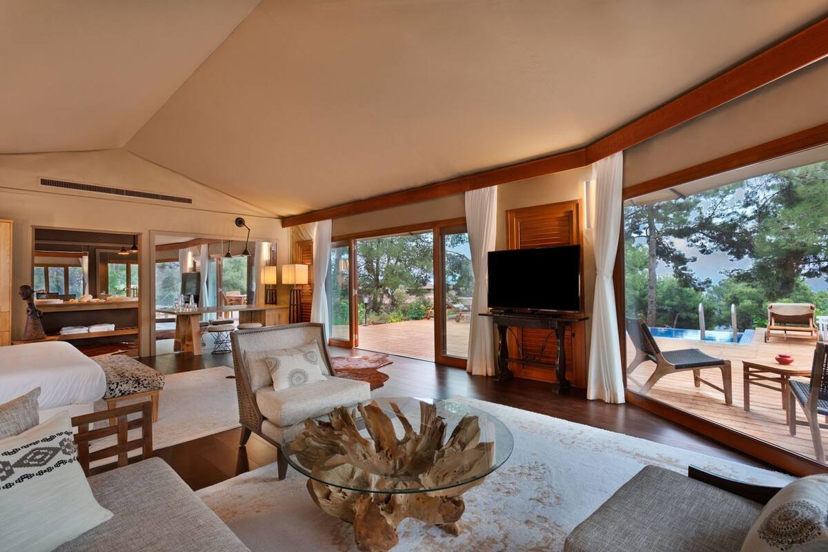 A spacious room with a large bed, a glass coffee table, a TV, and a view of the outdoors.