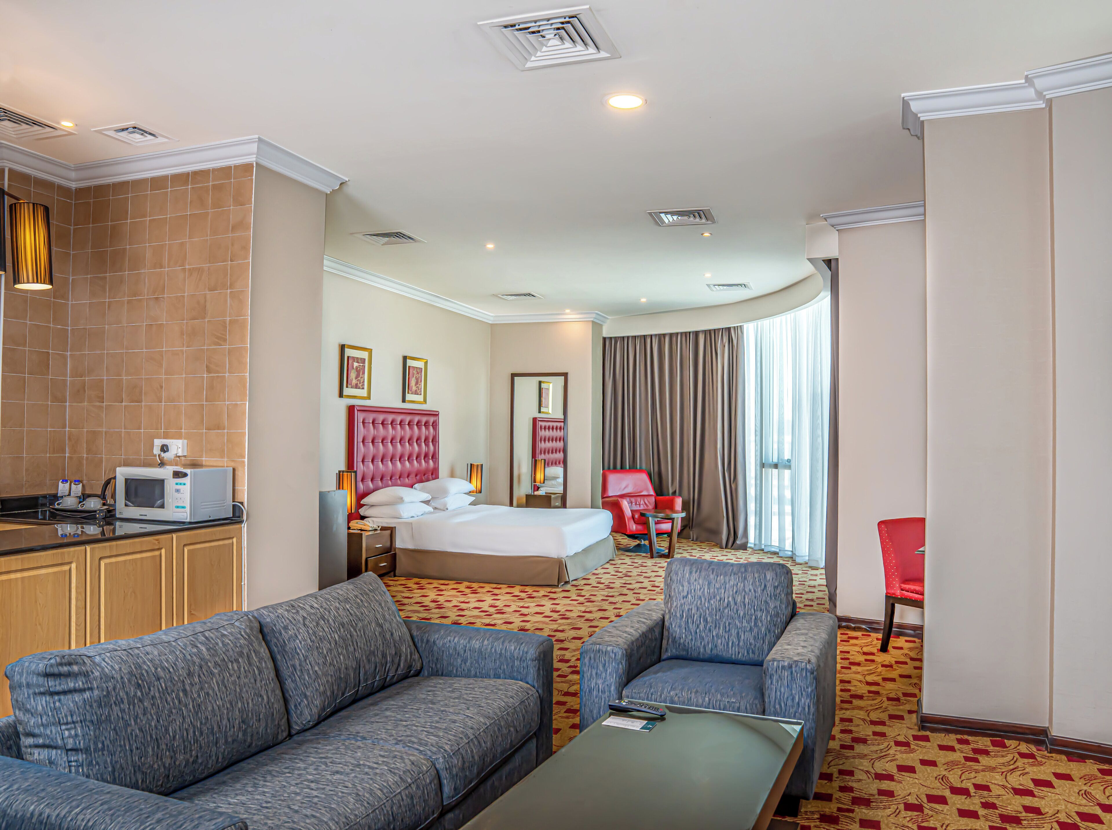 A hotel room with a bed, a sitting area with a sofa and armchair, a small table, a microwave, and a red chair.