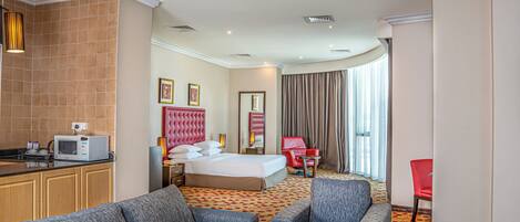 A hotel room with a bed, a sitting area with a sofa and armchair, a small table, a microwave, and a red chair.