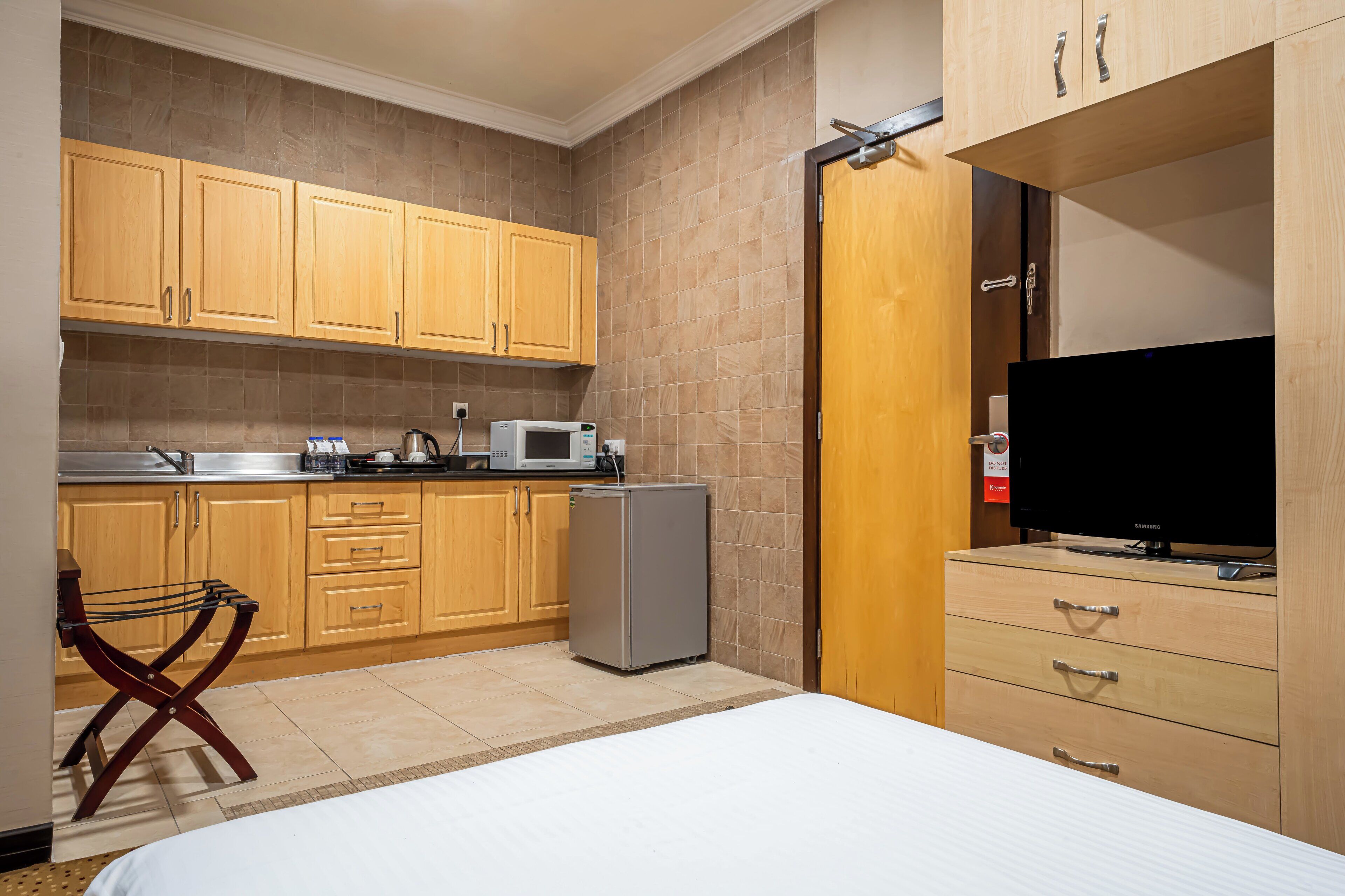 Habitación de hotel compacta con kitchenette, cama, televisión y armario de madera.