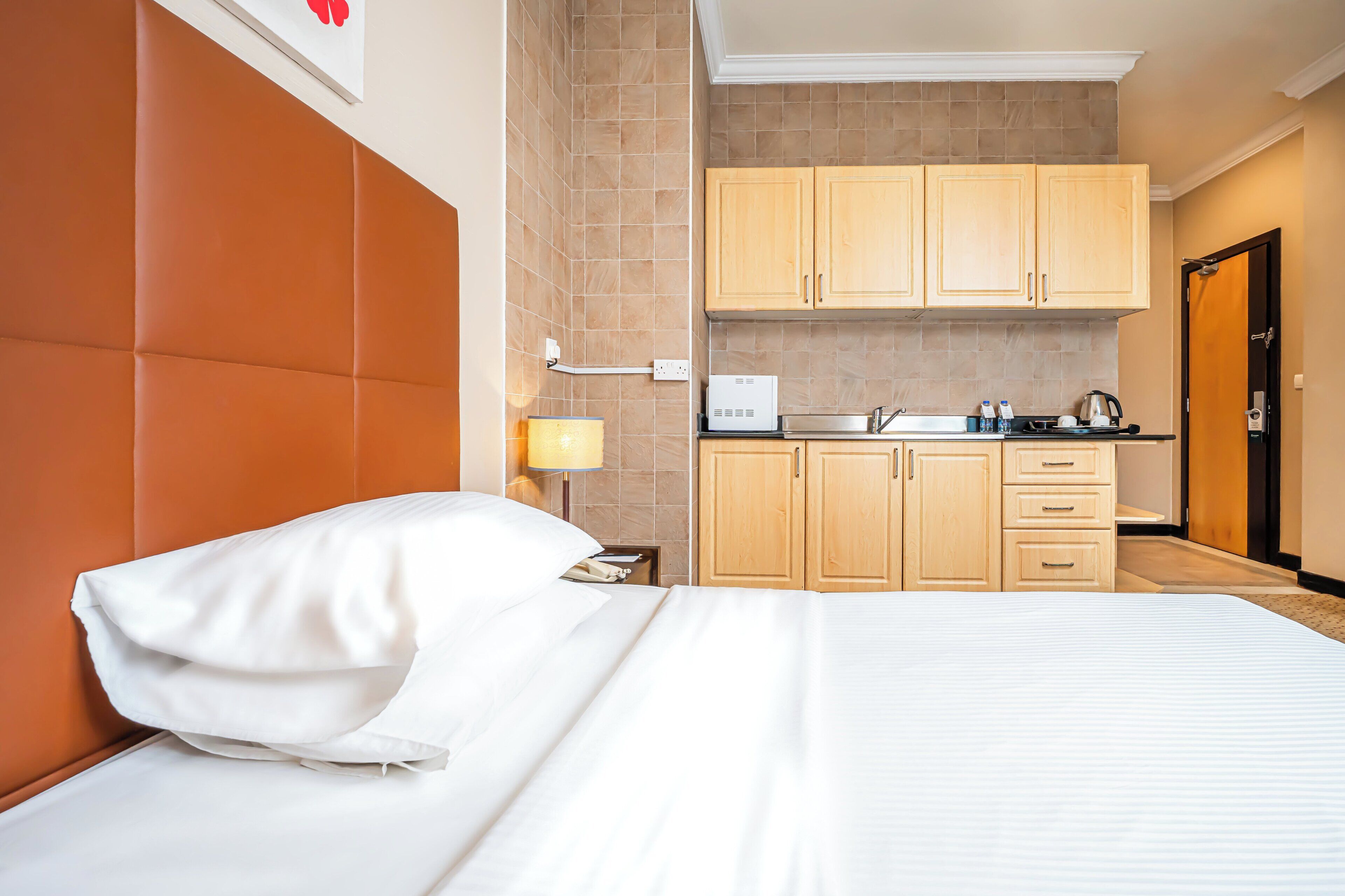 Una habitación de hotel con cama, mesita de noche, lámpara, kitchenette y armarios de madera.