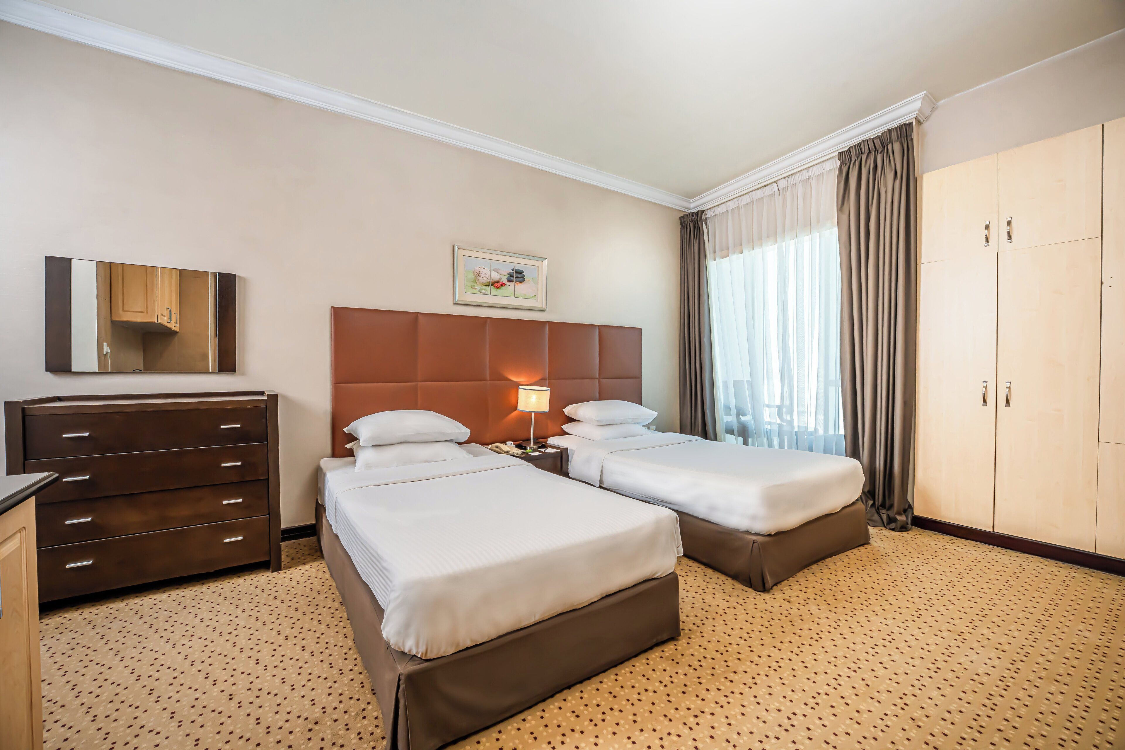 Habitación de hotel con dos camas, un aparador, cabecero, lámpara, un cuadro y un armario.