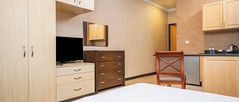 Una habitación de hotel con una cama, televisión, cómoda de madera, silla y kitchenette.