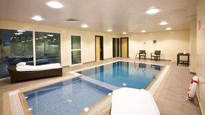 Una piscina interior con zona de estar, asientos y vistas al exterior.