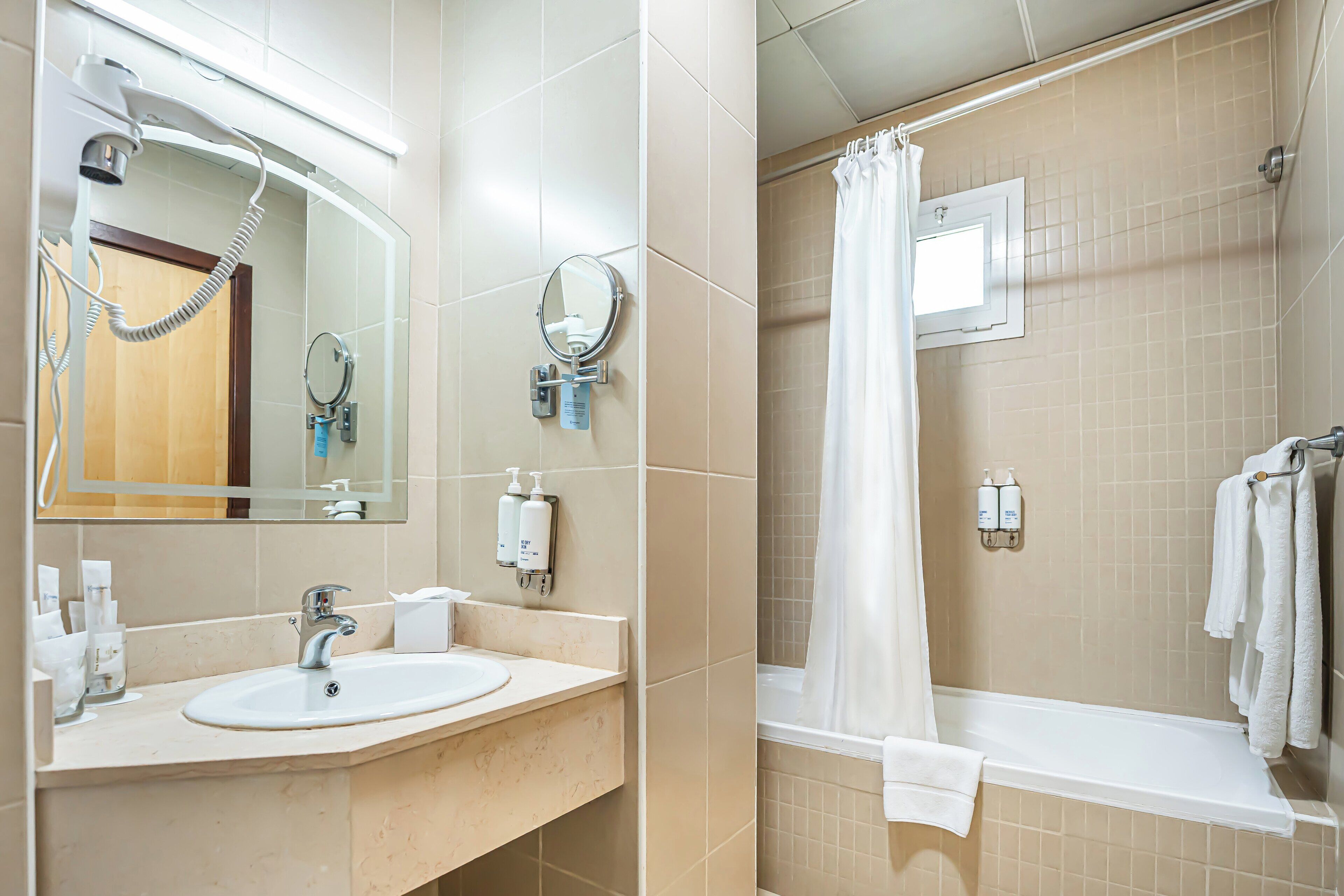 Un baño con lavamanos, espejo, secador de pelo y cortina de ducha.
