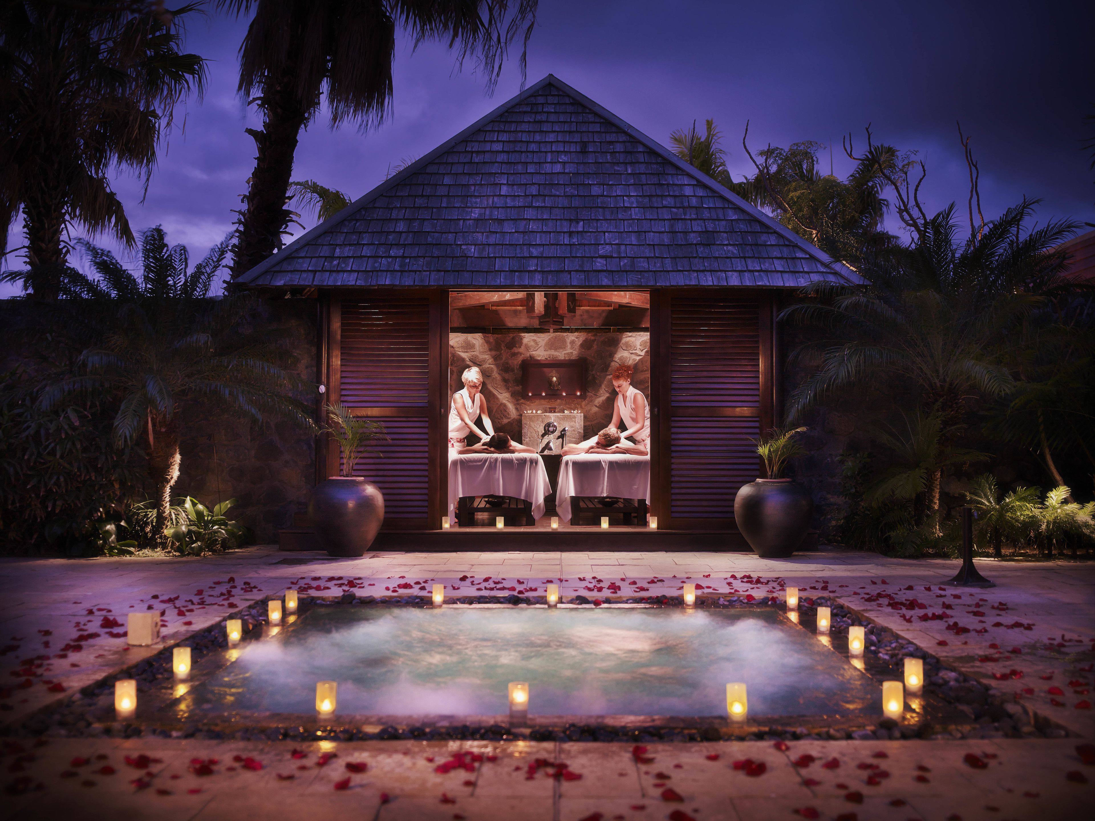 A spa with a massage table, a stone wall, and a water feature with candles.