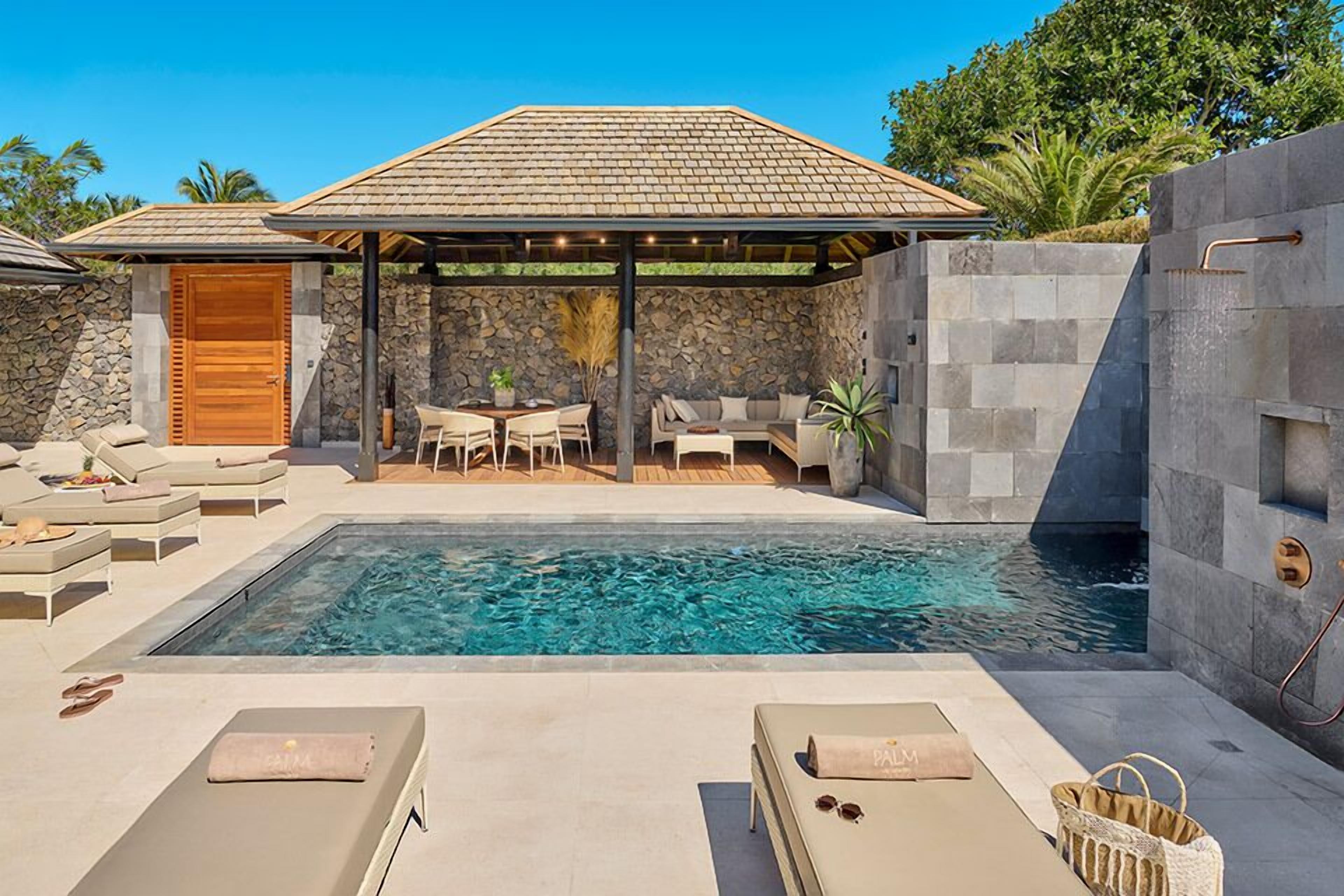 A pool area with lounge chairs, a covered seating area, and a stone wall.