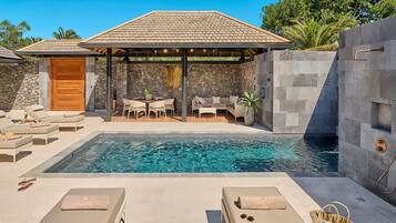 A pool area with lounge chairs, a covered seating area, and a stone wall.